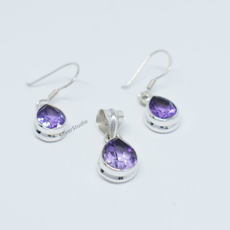 May include: A silver pendant and earrings set with a teardrop-shaped amethyst gemstone. The pendant and earrings have a silver bezel setting.
