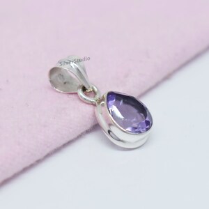 May include: A silver pendant with a purple amethyst gemstone. The pendant is shaped like a teardrop and has a simple design.