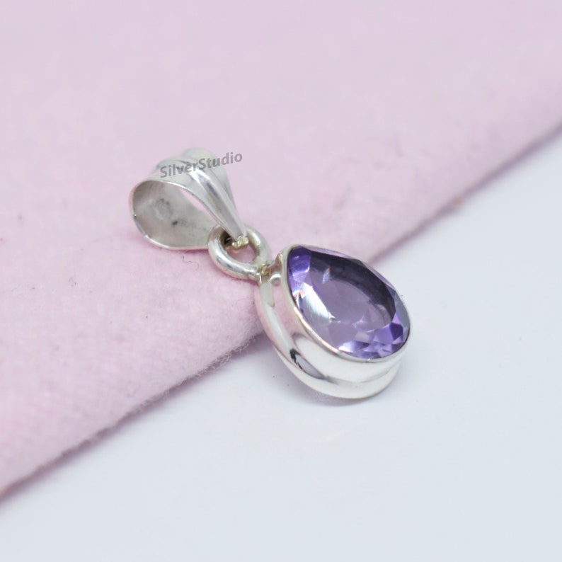 May include: A silver pendant with a purple amethyst gemstone. The pendant is shaped like a teardrop and has a simple design.