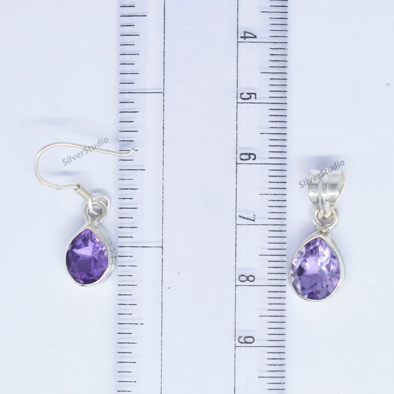 May include: A pair of sterling silver earrings and a pendant featuring a teardrop-shaped amethyst gemstone. The earrings are approximately 1 inch long and the pendant is approximately 1.5 inches long.