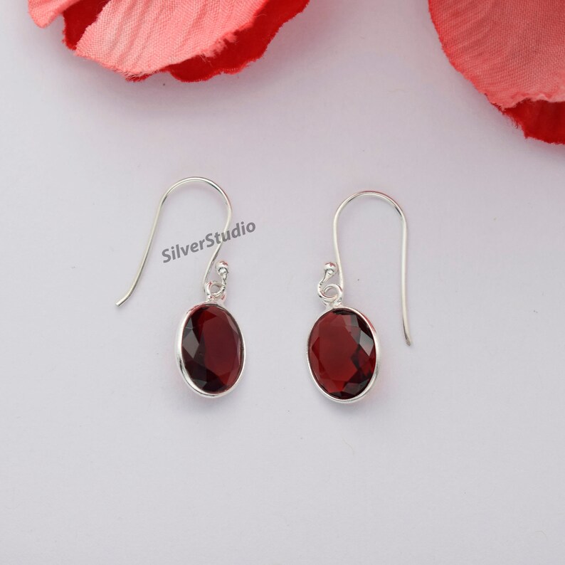 May include: A pair of silver earrings with red gemstone drops. The earrings have a simple design and are perfect for everyday wear.