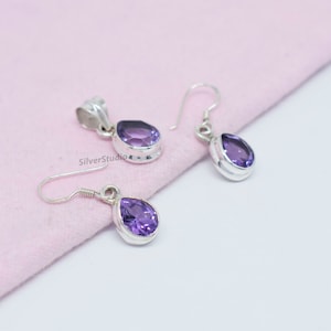 May include: A set of sterling silver earrings and a pendant featuring a teardrop-shaped amethyst gemstone. The earrings have a hook closure.