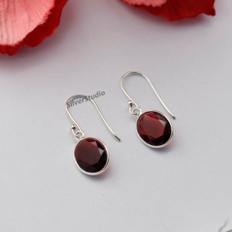 May include: A pair of silver dangle earrings featuring oval-shaped red gemstones. The earrings have a simple design and are ideal for everyday wear.