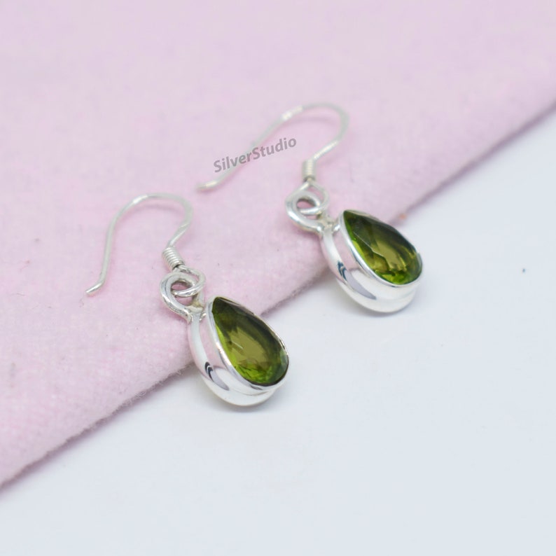 May include: A pair of silver earrings with green pear-shaped gemstones. The earrings have a simple design and are perfect for everyday wear.