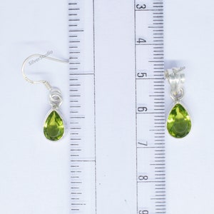 May include: A pair of silver earrings with green pear-shaped gemstones. The earrings are approximately 1.5 inches long.