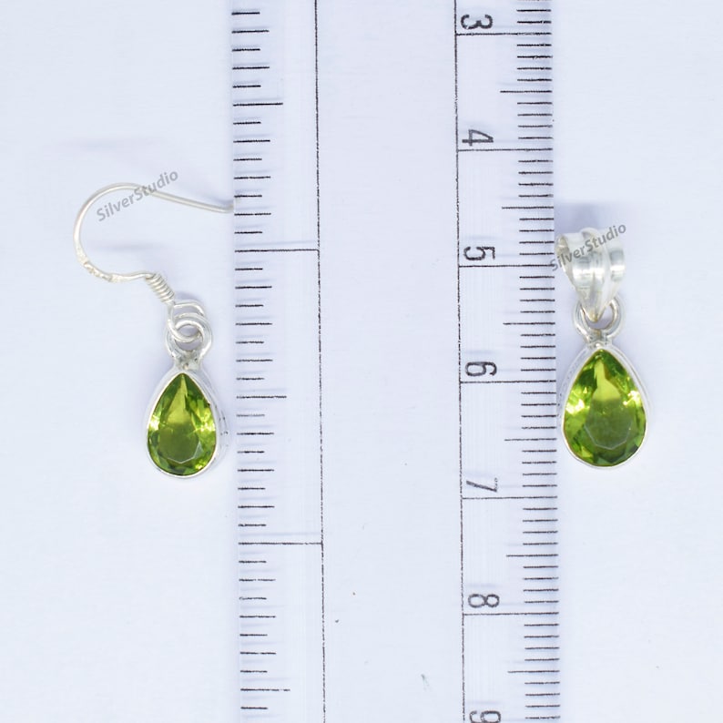 May include: A pair of silver earrings with green pear-shaped gemstones. The earrings are approximately 1.5 inches long.