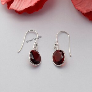 May include: A pair of silver dangle earrings featuring red oval-shaped gemstones. The earrings have a simple design and are ideal for everyday wear.