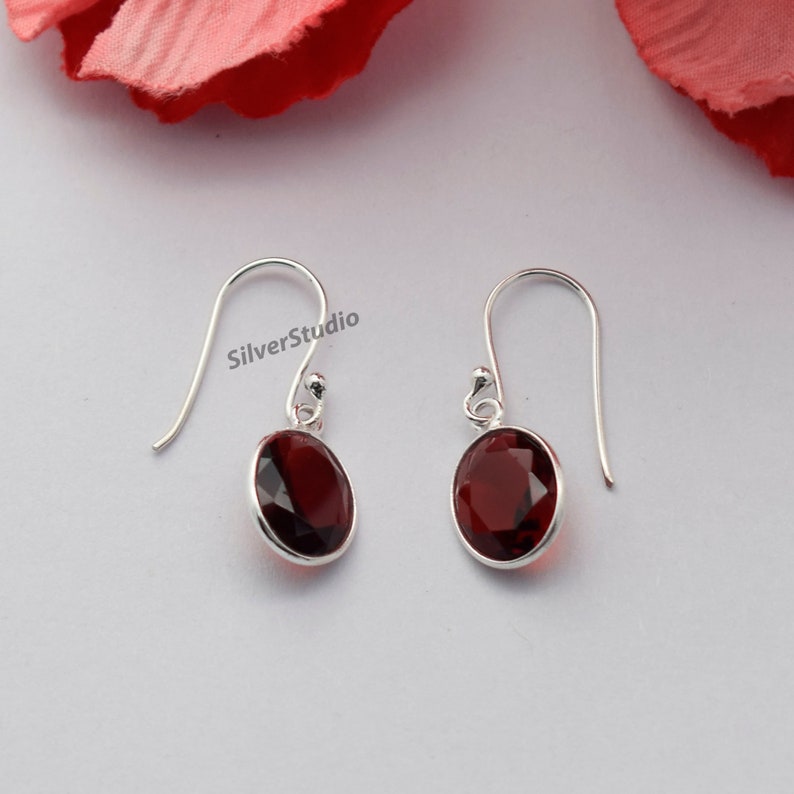 May include: A pair of silver dangle earrings featuring red oval-shaped gemstones. The earrings have a simple design and are ideal for everyday wear.