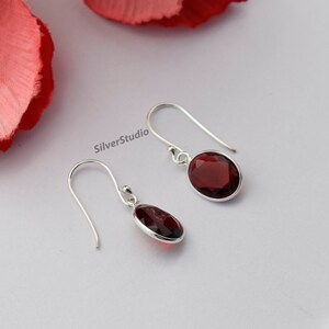 May include: A pair of silver dangle earrings featuring red oval-shaped gemstones. The earrings have a simple design and are ideal for everyday wear.