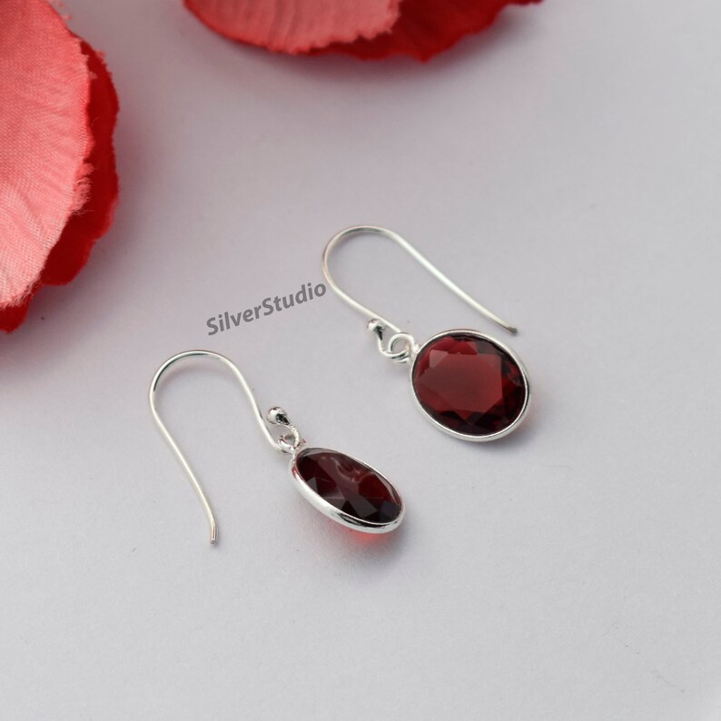 May include: A pair of silver dangle earrings featuring red oval-shaped gemstones. The earrings have a simple design and are ideal for everyday wear.