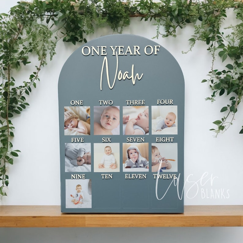 May include: A grey wooden arch with the words "ONE YEAR OF Noah" at the top. The arch is divided into twelve sections, each with a number from one to twelve and a photo of a baby.