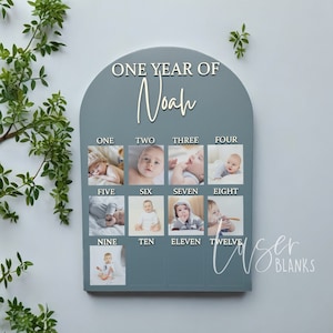 May include: A blue wooden photo display with the text "ONE YEAR OF Noah" at the top. There are twelve photo slots, each labelled with a number from one to twelve. Each slot has a photo of a baby boy.