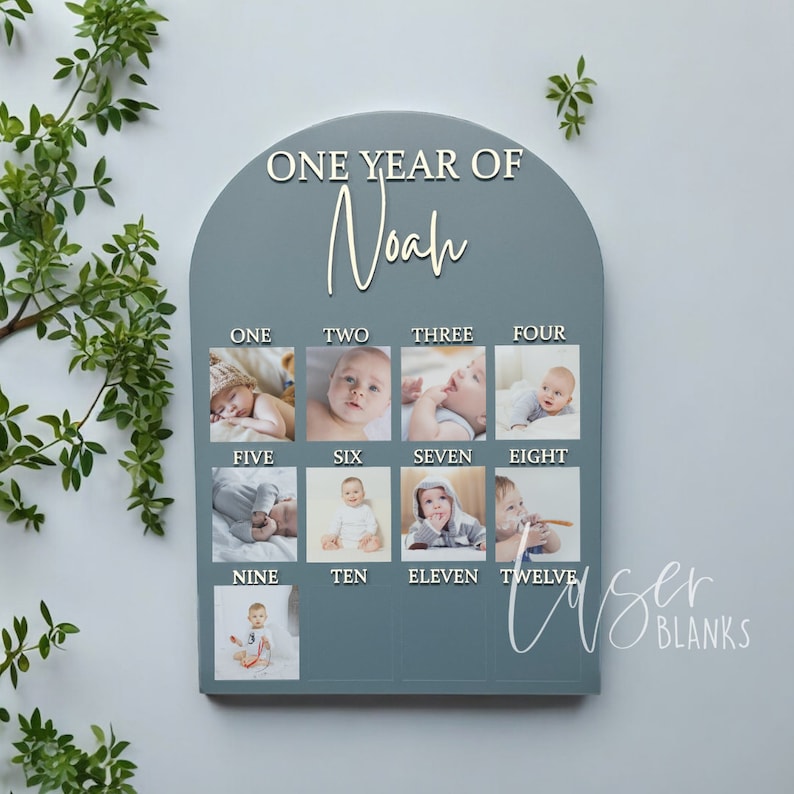 May include: A blue wooden photo display with the text "ONE YEAR OF Noah" at the top. There are twelve photo slots, each labelled with a number from one to twelve. Each slot has a photo of a baby boy.