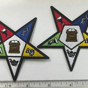May include: Two embroidered patches in the shape of a five-pointed star. The stars are black with white, red, blue, green, and yellow sections. Each section has a different symbol embroidered in black.