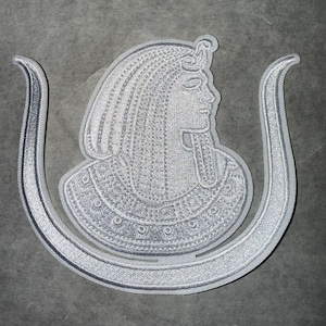 May include: A white embroidered patch of an Egyptian goddess with a cobra on her head, surrounded by a white embroidered snake design.