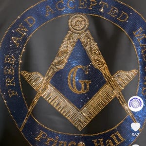 May include: A blue and gold Masonic symbol with the words "Free and Accepted Masons" and "Prince Hall" around the perimeter. The symbol is made of rhinestones and is on a black background.