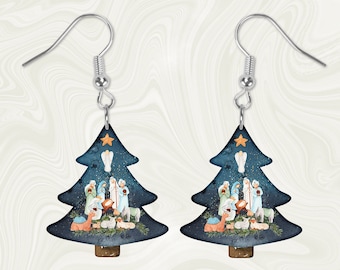 May include: A pair of silver dangle earrings with a blue and gold Christmas tree design. The tree features a star on top and a nativity scene with figures of Mary, Joseph, and baby Jesus.
