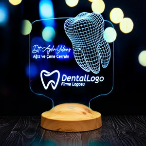May include: A blue and white 3D printed acrylic lamp with a tooth design. The lamp has a wooden base and features the text "Dr. Aydin Yilmaz Agiz ve Cene Cerrahi DentalLogo Firma Logosu".