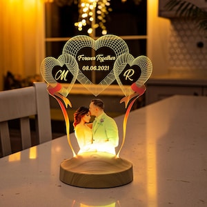 Könnte beinhalten: Ein Holzsockel mit einer leuchtenden, herzförmigen Acryllampen mit einem Foto eines Paares und dem Text "Forever Together 08.06.2021" in der Mitte.