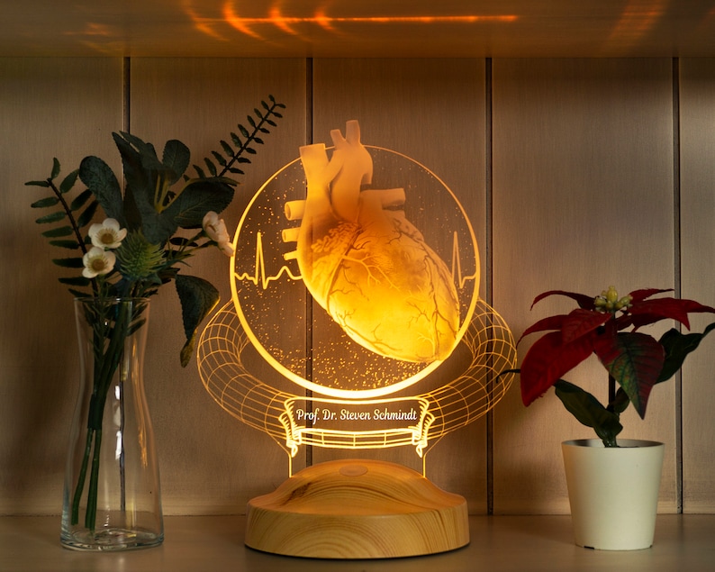 The lamp is shown on the front side in this photo. There are flowers in a vase on either side of the lamp. The lamp is shines orange.