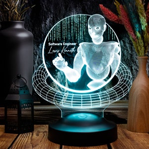May include: A 3D printed, blue and white,  LED night light with a geometric design. The light features a stylized image of a person with the text "Software Engineer Lewis Kenneth" on the front.