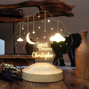 May include: A wooden night light shaped like a cloud with a crescent moon, stars, and clouds hanging from it. The light has the text "Sweet Dreams Christopher" on it.