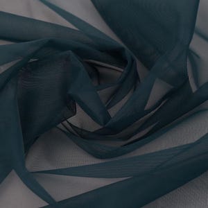 May include: Close-up of a dark teal sheer fabric with a delicate, flowing texture. The fabric is draped and folded, creating shadows and highlights. The material appears lightweight and airy, suitable for curtains or apparel.