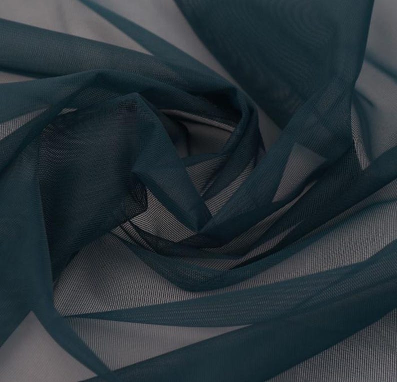May include: Close-up of a dark teal sheer fabric with a delicate, flowing texture. The fabric is draped and folded, creating shadows and highlights. The material appears lightweight and airy, suitable for curtains or apparel.