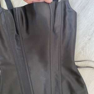 May include: A black satin corset with boning and adjustable straps. The corset has a low neckline and a pointed bottom.