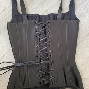 May include: Black satin corset with a lace-up back and adjustable straps. The corset has a boned structure and a smooth, sleek finish.