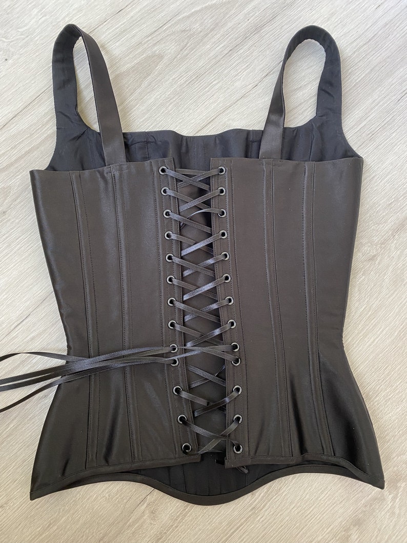May include: Black satin corset with a lace-up back and adjustable straps. The corset has a boned structure and a smooth, sleek finish.