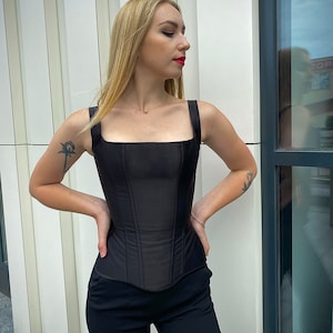 May include: A black corset with a square neckline and boning details. The corset is made of a smooth, satin-like fabric.