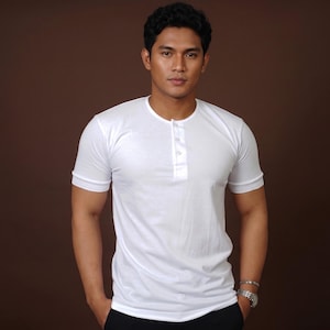 May include: A short-sleeved white henley shirt featuring a round neckline with a vertical placket containing three matching white buttons. The garment is constructed with a smooth fabric and has fitted sleeves with a subtle ribbed hem detail.