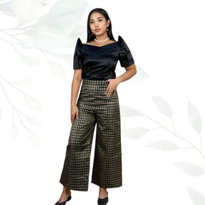 May include: A woman in a black satin top with a square neckline and short sleeves. She is wearing wide-leg trousers with a gold and black woven pattern. The outfit is a formal style.