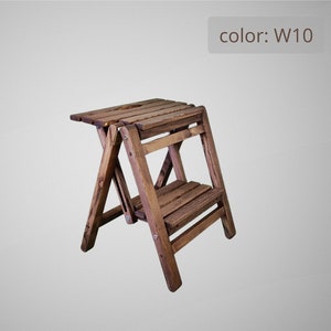 Può includere: Uno sgabello in legno marrone con due gradini. Lo sgabello è ripiegato e pronto per l'uso. Il colore dello sgabello è W10.