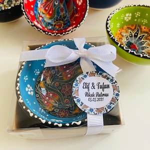 May include: A set of small, colorful ceramic bowls with intricate floral designs. The bowls are packaged in a clear box with a white ribbon and a round tag that reads "Elif & Tufan Nikah Hatırası 05.03.2021".