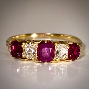 May include: A gold band ring featuring three red rubies and two diamonds. The rubies are set in a square shape and the diamonds are round.
