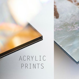 May include: Close-up of the edge of two acrylic prints. The print on the left has a rainbow-like sheen. The print on the right has a light blue and white abstract design. The text "ACRYLIC PRINTS" is printed below the images.