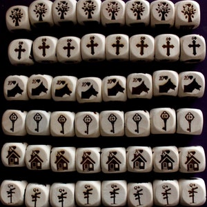 Peut inclure: Un ensemble de 40 dés en bois avec différents symboles, notamment des arbres, des croix, des maisons, des clés et une empreinte de patte de chien. Les dés sont disposés en rangées sur une surface violette.