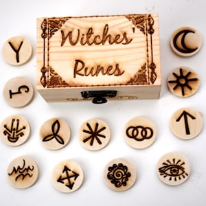 Può includere: Una scatola di legno con le parole "Witches' Runes" incise sul coperchio. La scatola contiene 15 rune di legno con vari simboli e lettere incisi su di esse.