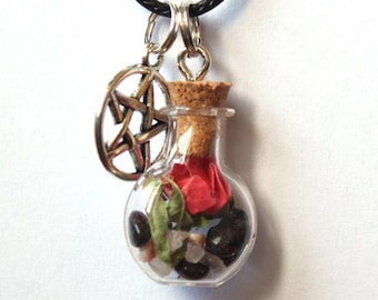 Puede incluir: Collar con colgante de vial de vidrio transparente con tapón de corcho, relleno de piedras negras y transparentes, pétalos rojos y hojas verdes. Un dije de pentagrama plateado cuelga junto al vial. El collar tiene un cordón negro.