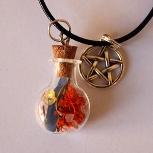 May include: A black cord necklace with a glass bottle pendant filled with orange and white crystals and a silver pentagram charm.