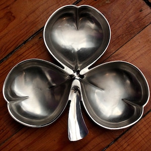 May include: A silver shamrock-shaped dish with three sections. The dish is made of metal and has a shiny finish.