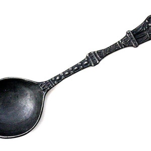 Peut inclure: Une cuillère en argent avec un manche orné d'un motif détaillé de deux personnages. La cuillère a un bol arrondi et une finition polie.