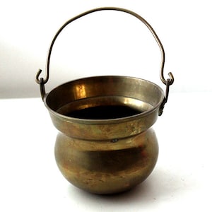 May include: A small, brass pot with a handle. The pot is round and has a slightly flared lip. It is made of a shiny, polished brass.