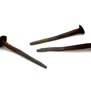 Peut inclure: Trois clous en fer rouillés avec des têtes carrées. Les clous sont disposés en forme de triangle sur un fond blanc.