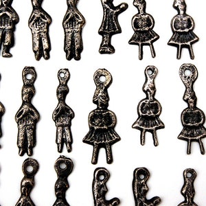 Op de afbeelding: Een verzameling vintage metalen bedels met verschillende figuren, waaronder mensen, dieren en abstracte ontwerpen. De bedels zijn gemaakt van donker metaal met een verweerde, antieke afwerking.