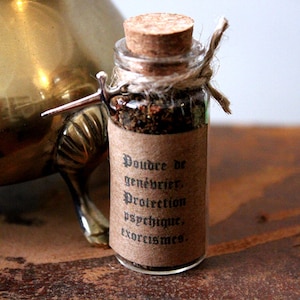 Può includere: Una piccola bottiglia di vetro con un tappo di sughero e un'etichetta di carta marrone. L'etichetta recita "Poudre de genévrier, Protection psychique, exorcismes".