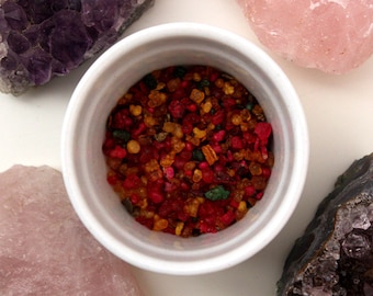 May include: A white ceramic bowl filled with a mixture of red, orange, yellow, and green incense chips.