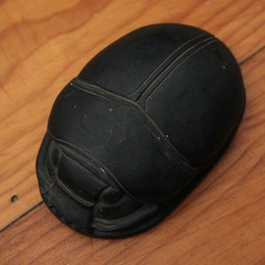 Puede incluir: Una escultura de escarabajo negro con detalles intrincados. La escultura est&aacute; hecha de un material liso y oscuro y tiene un acabado brillante.